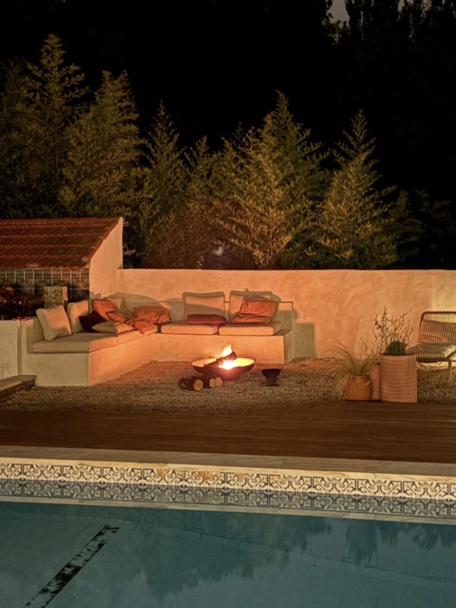 Firepit lounge glowing beside the villa pool at night